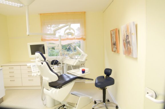 Behandlungsraum mit Zahnarztstuhl, Monitor und bunten Bildern an der Wand.